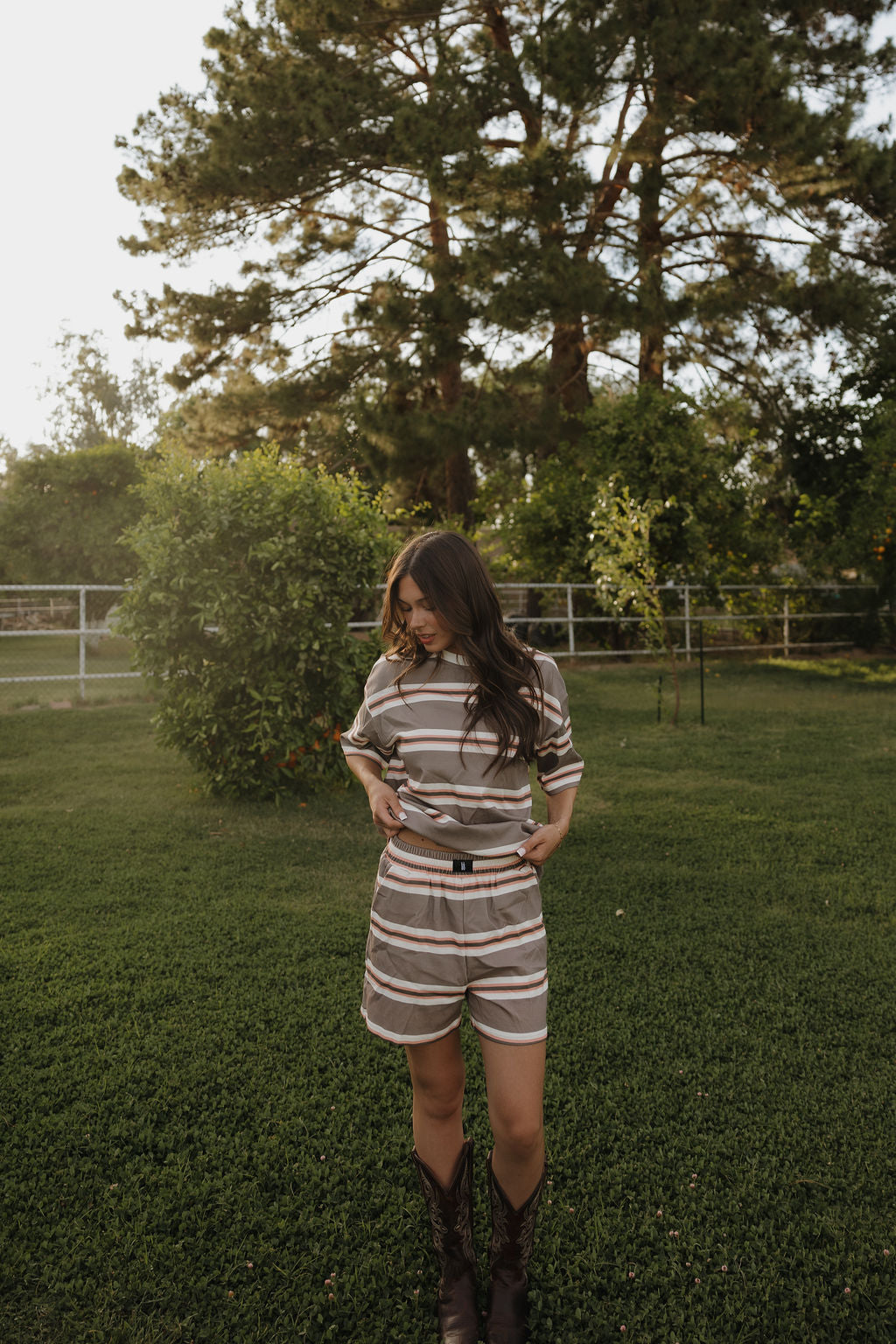 Woman in a striped outfit standing in a grassy area with trees in the background