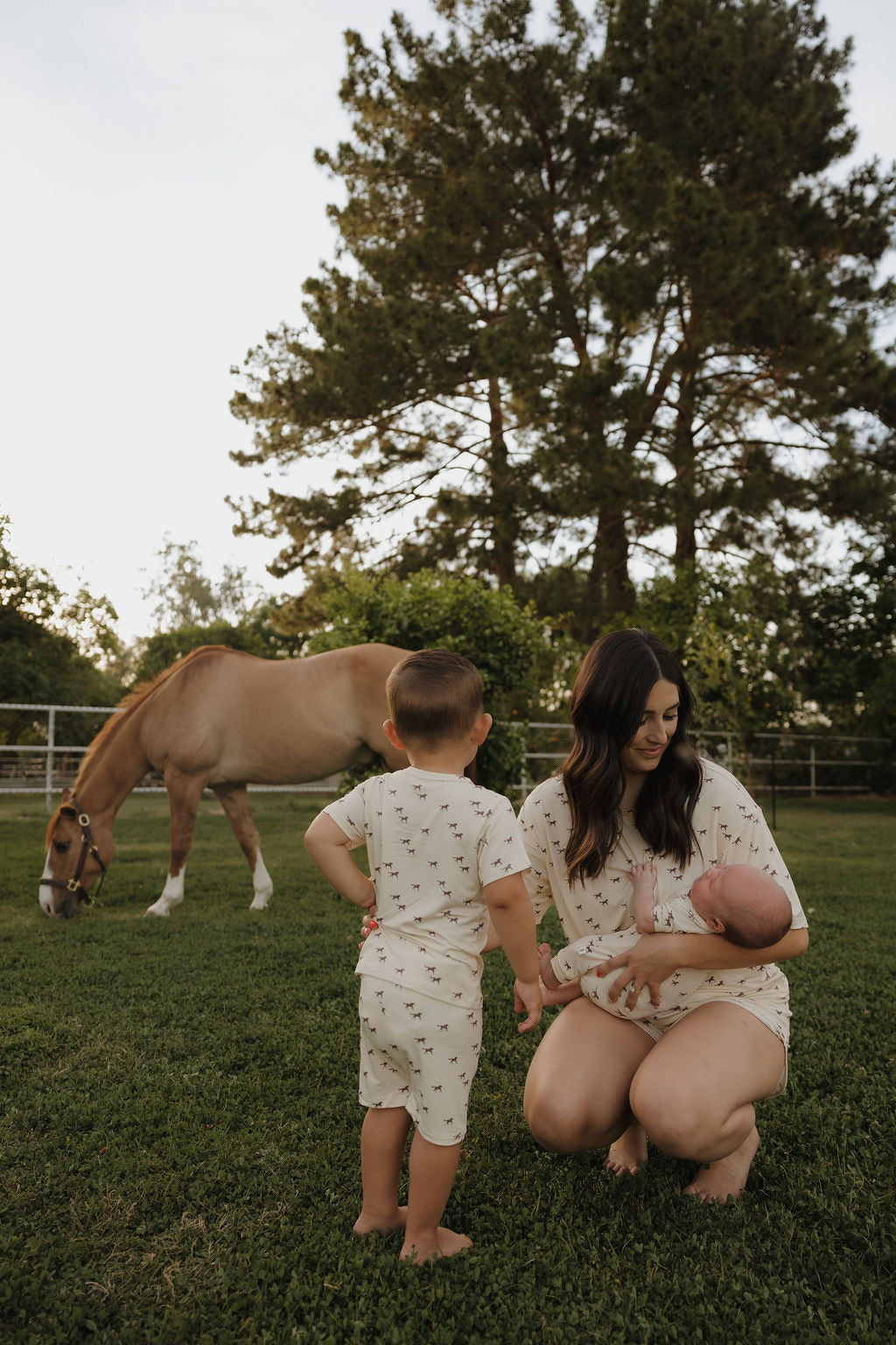 Woman and child in a grassy field with a horse in the background