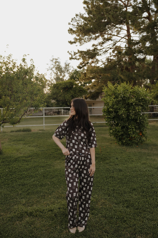 Woman in a patterned outfit standing in a grassy area with trees in the background