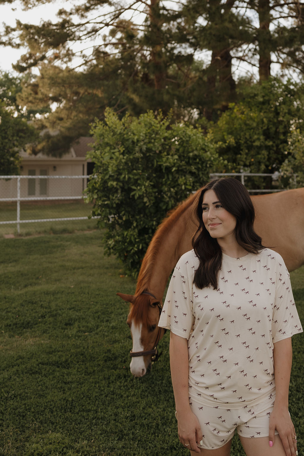 Woman standing next to a horse in a grassy field with trees in the background