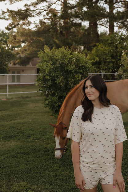 Woman standing next to a horse in a grassy field with trees in the background