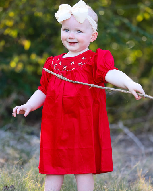 Child in a red dress holding a stick outdoors with greenery in the background