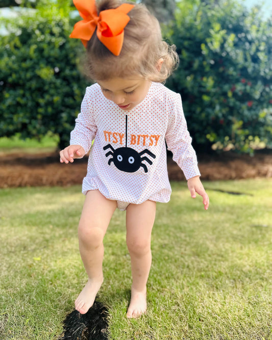 Child wearing a white outfit with a spider design and 'Yay Bitty' text, standing on grass.