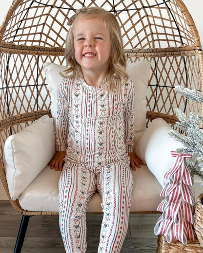 Child in patterned pajamas sitting in a wicker chair with a Christmas tree in the background