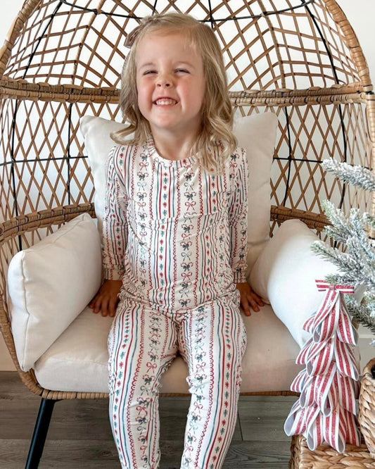 Child in patterned pajamas sitting in a wicker chair with a Christmas tree in the background