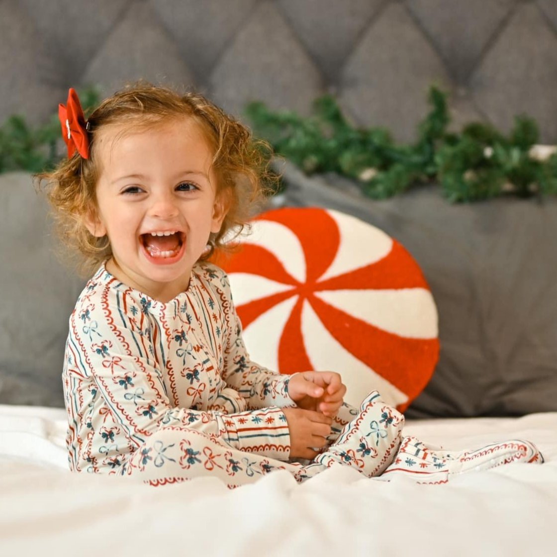 Child in pajamas sitting on a bed with a candy cane pillow