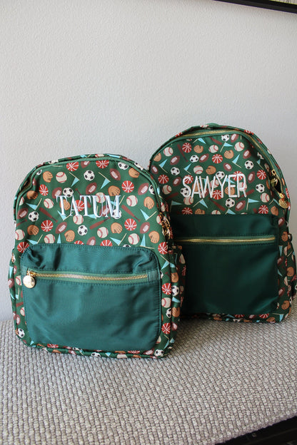 Two green backpacks with sports-themed patterns and embroidered names on a gray surface.