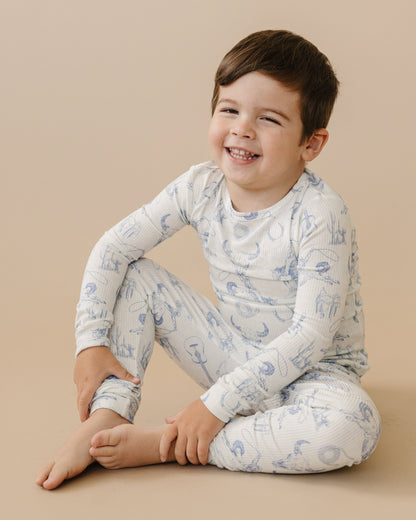 Child wearing a white long-sleeve shirt and pants with blue patterns on a beige background