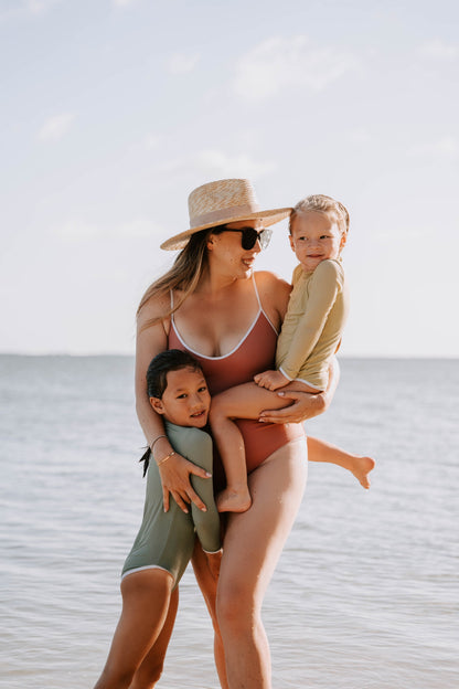 Woman in a swimsuit holding two children on a beach
