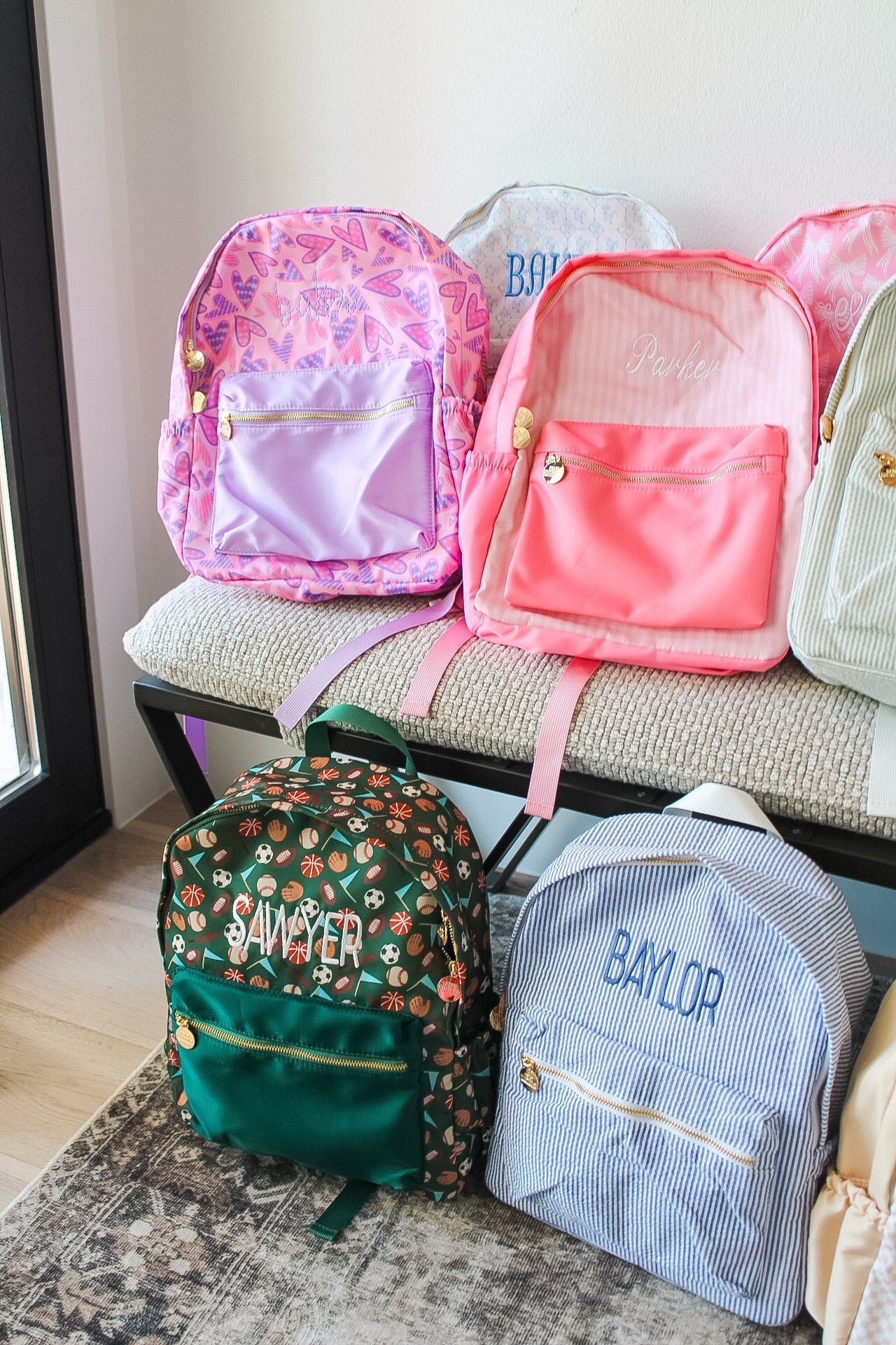 Collection of colorful backpacks on a bench with visible names.