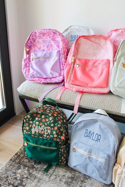 Collection of colorful backpacks on a bench with visible names.