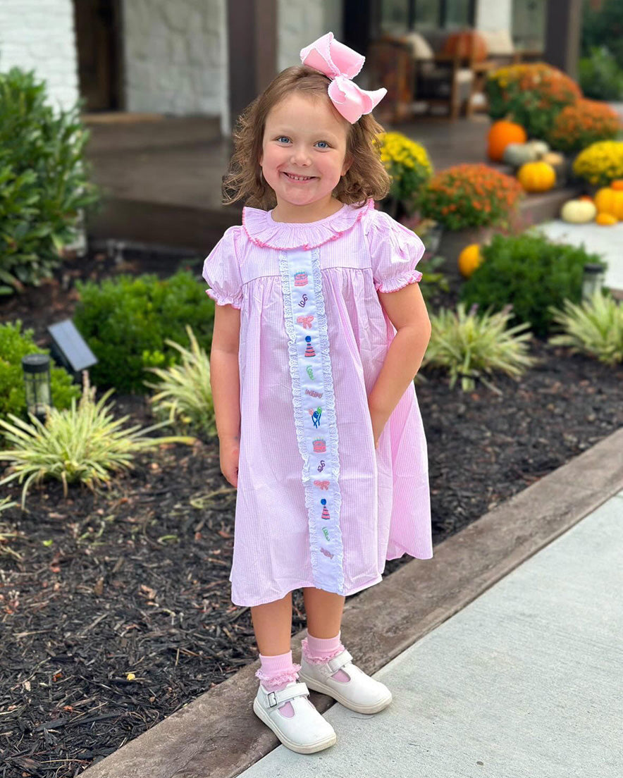 Young girl in a pink dress standing outdoors with flowers and pumpkins in the background