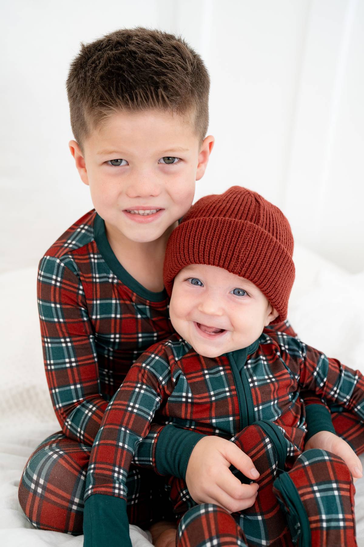 Two children wearing matching plaid outfits with a baby in a red hat.