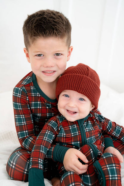 Two children wearing matching plaid outfits with a baby in a red hat.