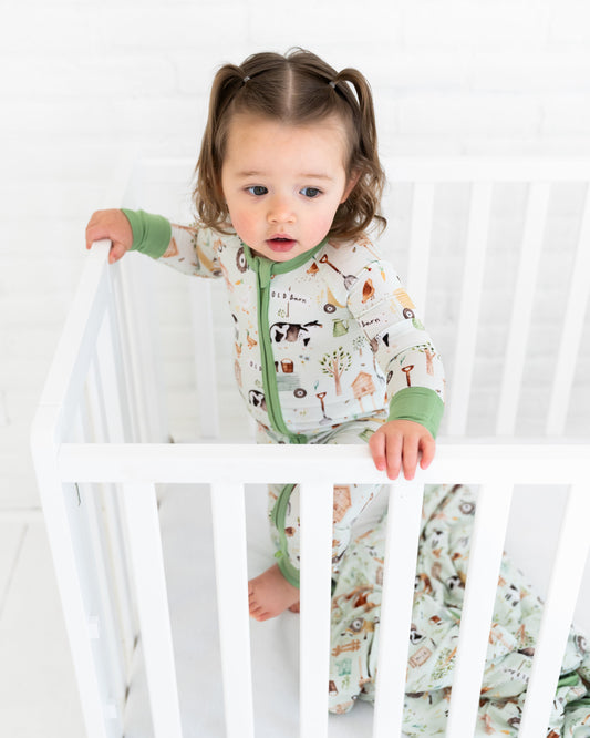 Child in a crib wearing a patterned onesie with green accents.