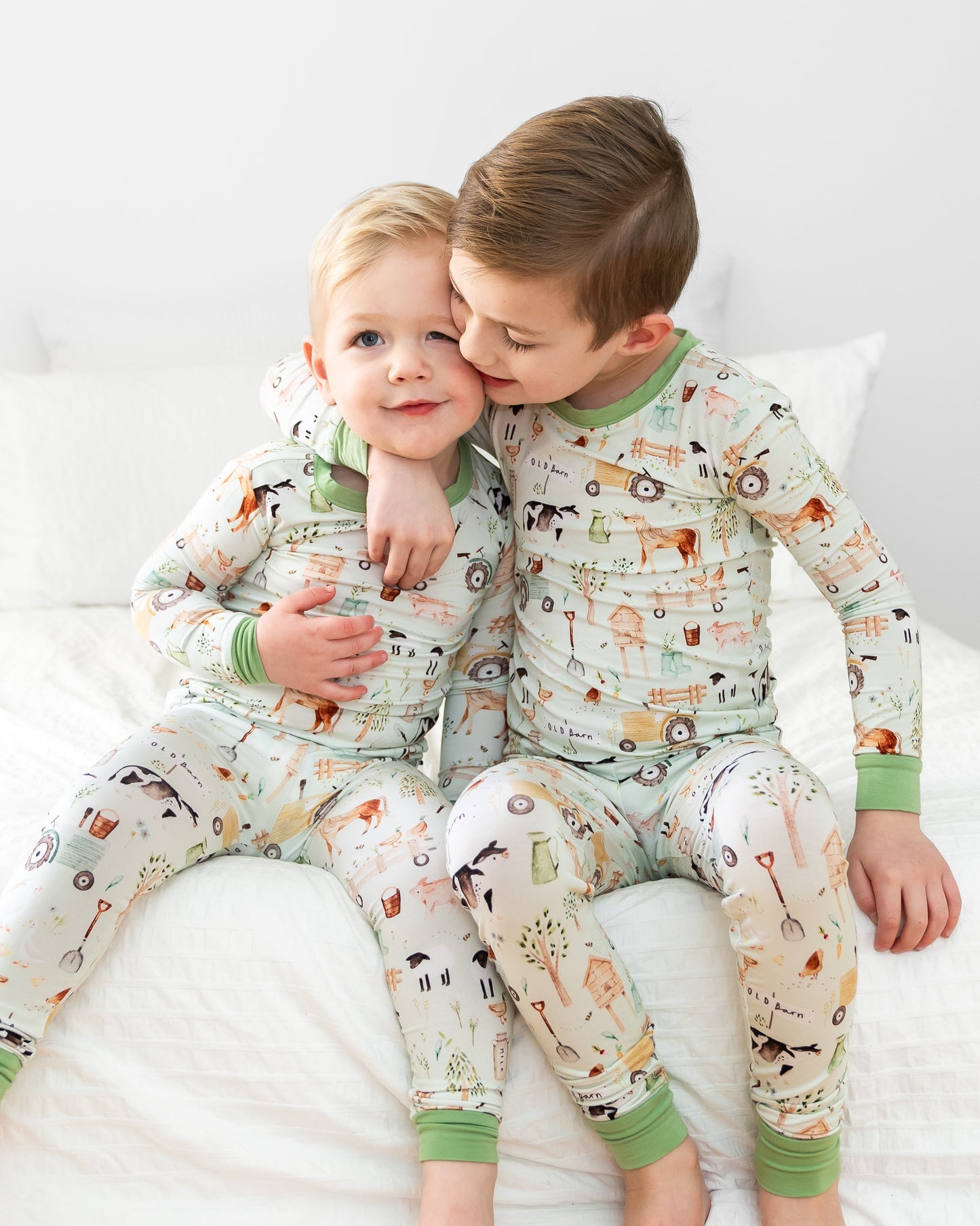 Two children in pajamas with animal patterns sitting on a white surface.