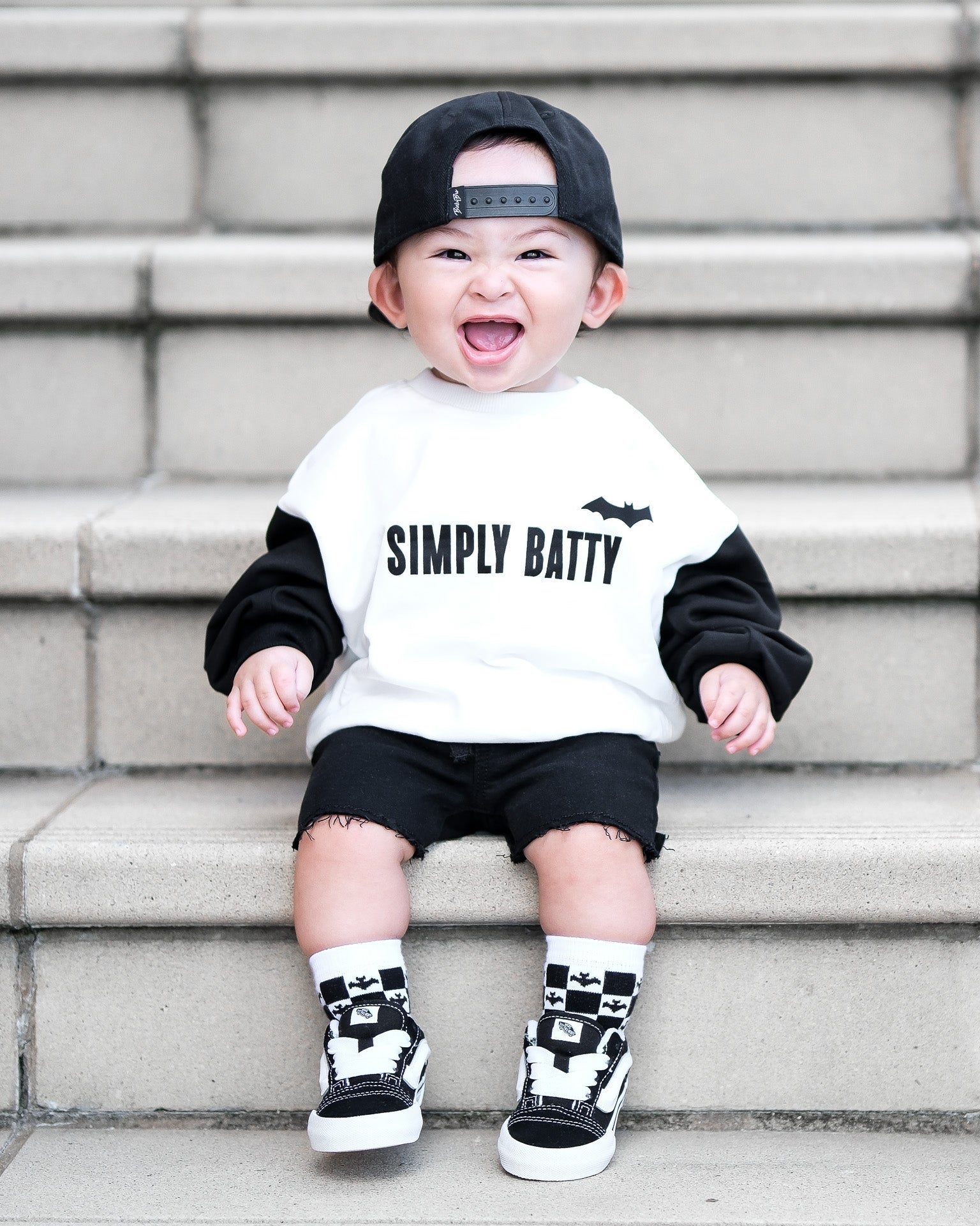 Child wearing a 'Simply Batty' shirt sitting on steps.