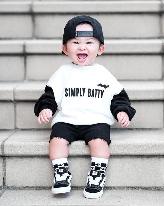 Child wearing a 'Simply Batty' shirt sitting on steps.