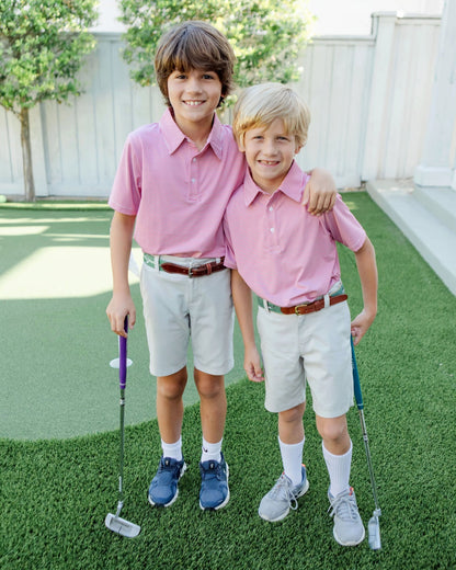 Two boys in red shirts and khaki shorts standing on a grassy area with golf clubs.