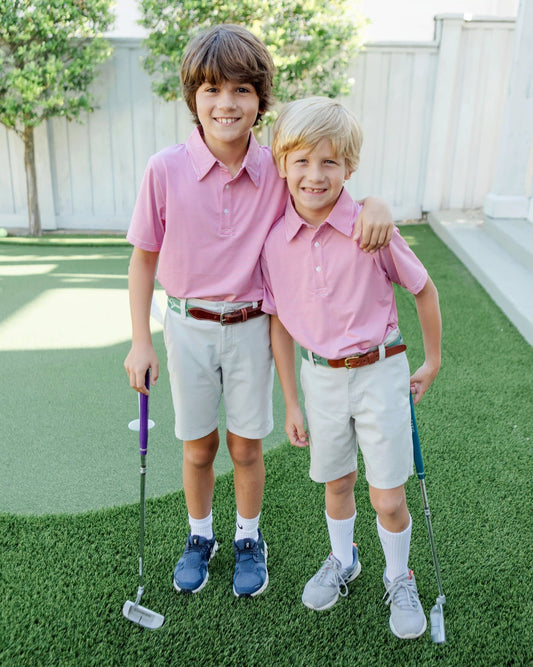 Two boys in red shirts and khaki shorts standing on a grassy area with golf clubs.