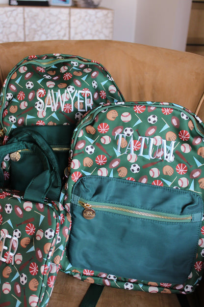 Three backpacks with sports-themed patterns and monograms on a wooden surface.