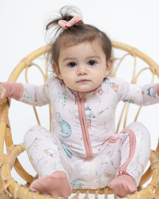 Baby sitting in a wicker chair wearing a pink and white outfit with animal prints.