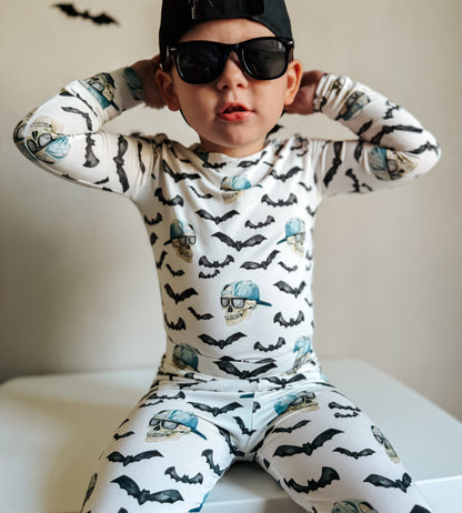 Child wearing a pajama set with bat patterns and sunglasses, sitting on a white surface.