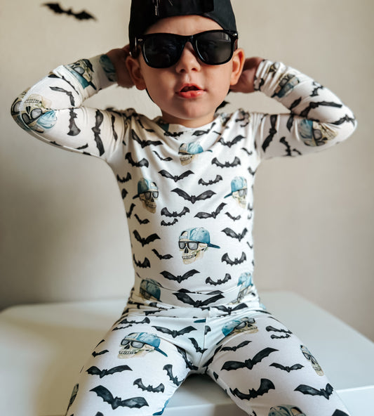 Child wearing a pajama set with bat patterns and sunglasses, sitting on a white surface.