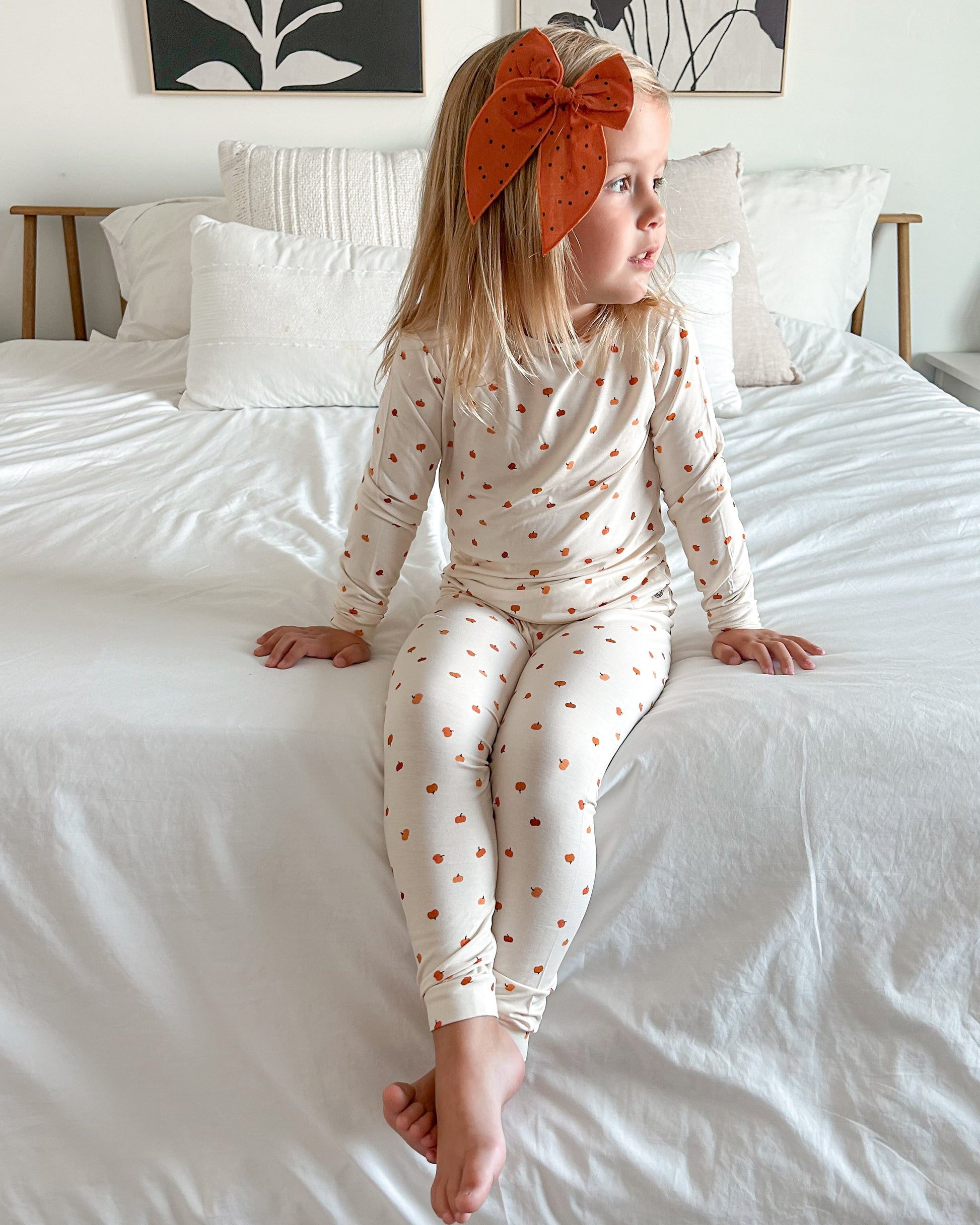 Child wearing a polka dot outfit sitting on a bed with floral wall art in the background