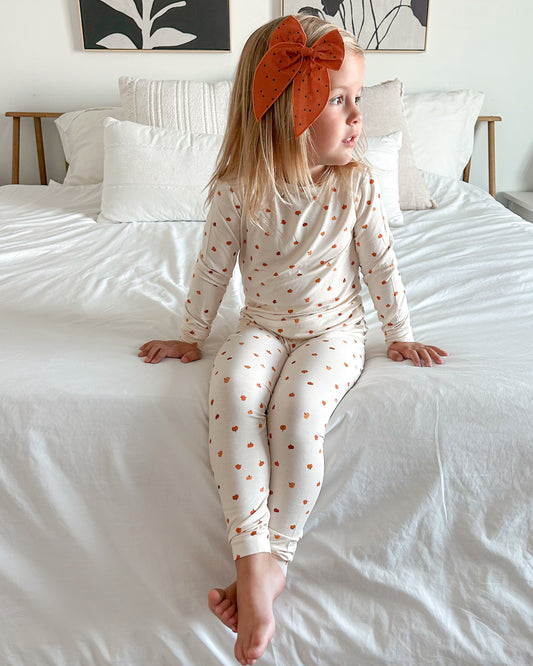 Child wearing a polka dot outfit sitting on a bed with floral wall art in the background