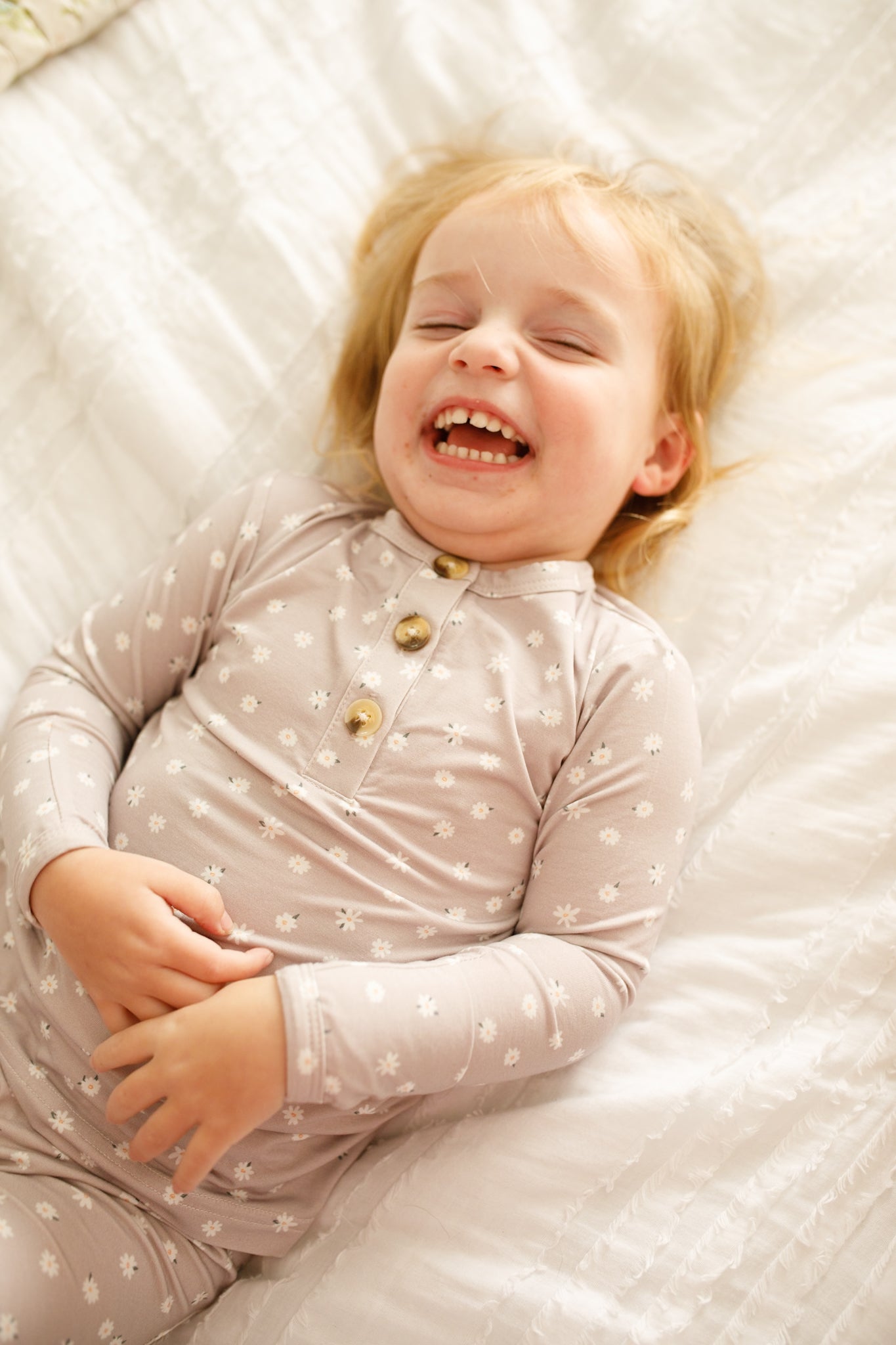 Child wearing a light pink polka dot outfit lying on a white quilted surface.