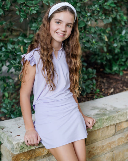 Young girl in a light purple set standing against a green leafy background