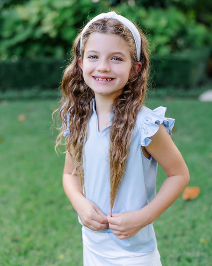 Young girl with long hair wearing a light blue sleeveless top with ruffled sleeves outdoors.