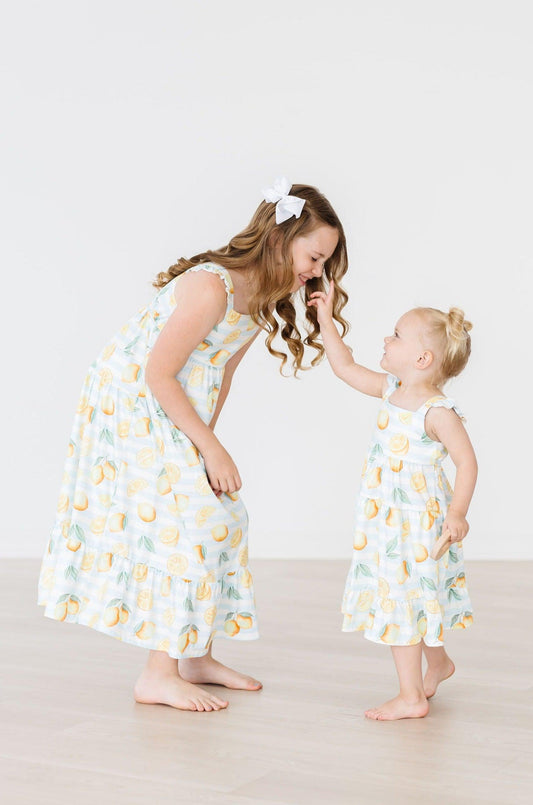 Two children wearing matching dresses with a lemon pattern on a plain background
