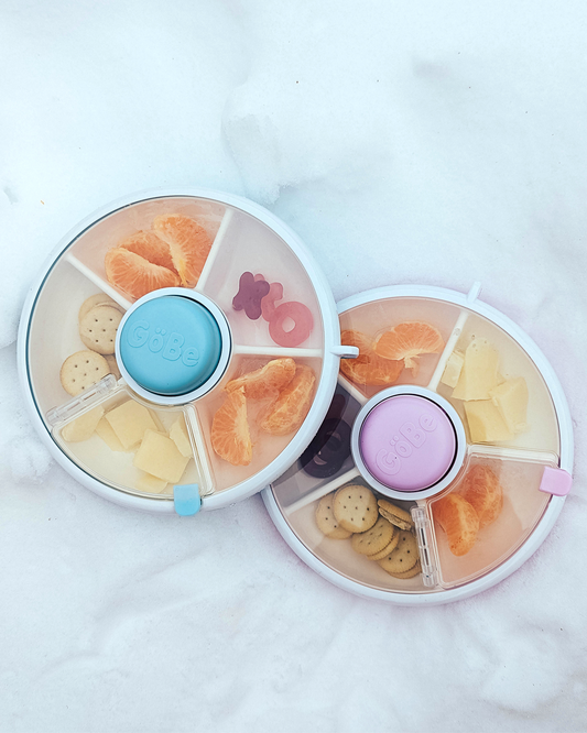 Round snack container with compartments filled with various snacks on a white background