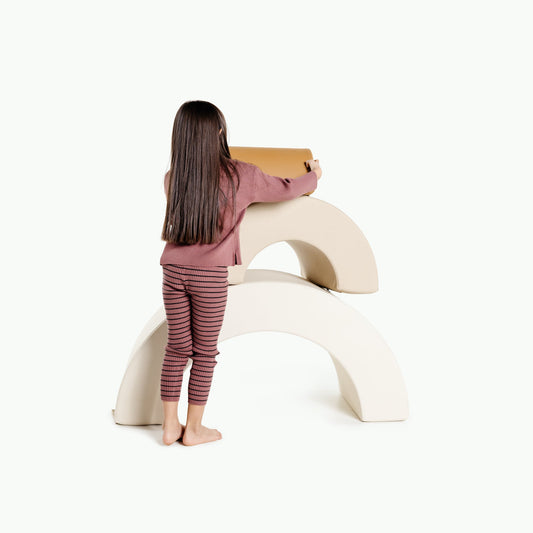 Child sitting on a white curved chair holding a cardboard box against a white background