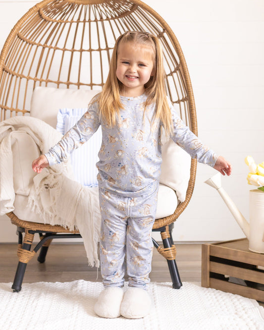 Young girl in pajamas standing in a cozy room with a wicker chair and decorative items.