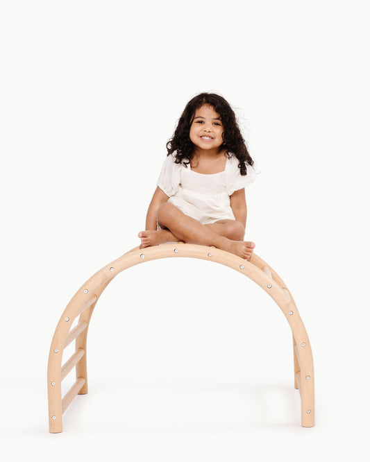Child sitting on a wooden arch toy against a white background