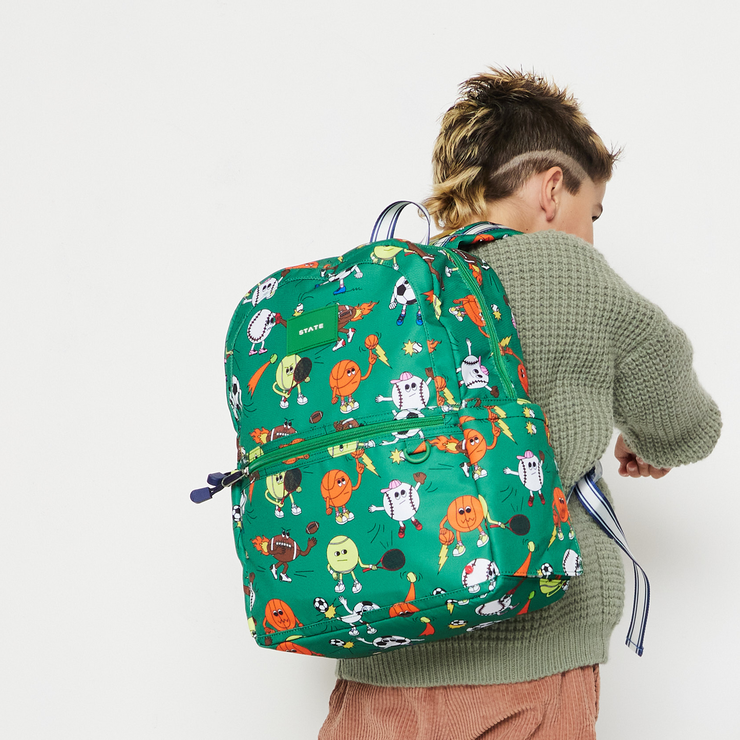 Child wearing a green backpack with colorful robot pattern on a white background