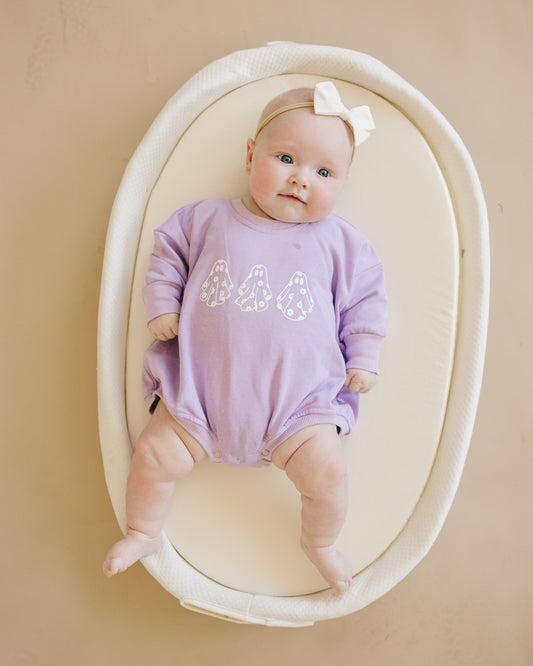 Baby in a purple outfit with 'ghosts' on a beige background