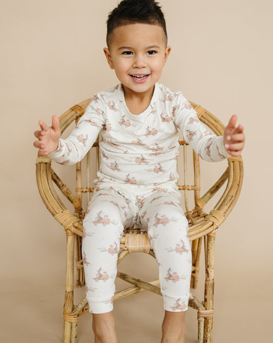 Child wearing a patterned outfit sitting on a wooden chair against a beige background