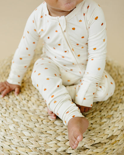 Baby in a white outfit with orange polka dots sitting on a woven mat.