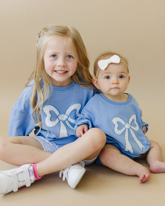 Two young children wearing matching blue outfits with bow designs on a beige background