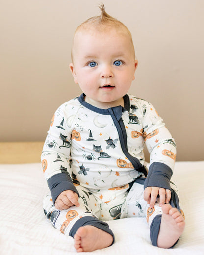 Baby wearing a Halloween-themed onesie sitting on a bed.