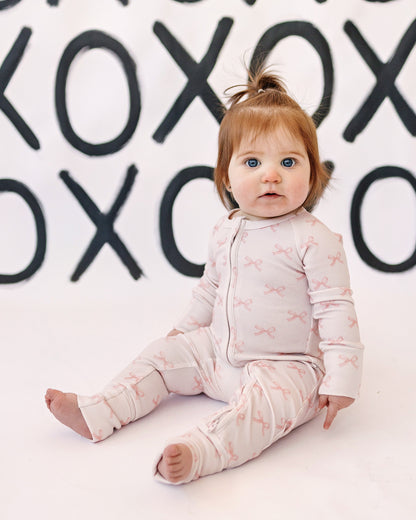 Baby sitting on a white floor with a background of black 'XO' patterns