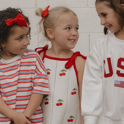 Three children wearing red and white outfits against a white brick wall.