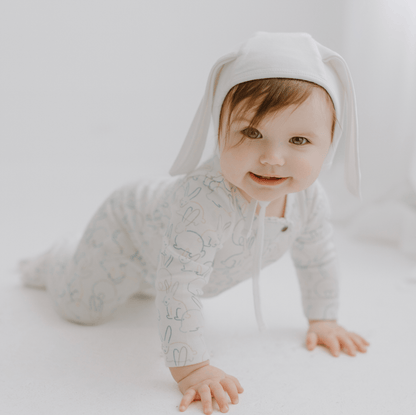 Baby wearing a light gray onesie with bunny ears on a white background
