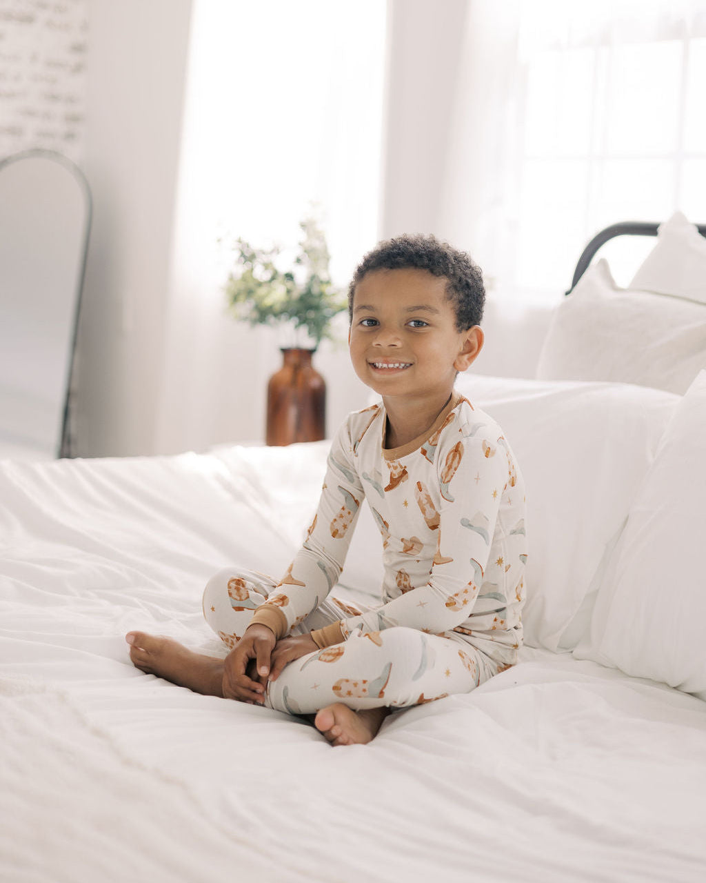 Child wearing pajamas sitting on a bed in a bright room