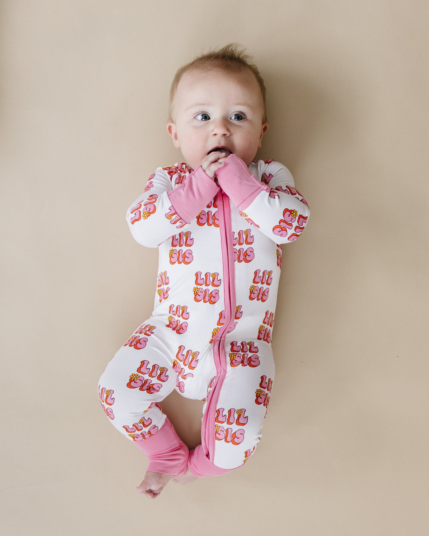 Baby wearing a white onesie with red text and pink accents on a beige background