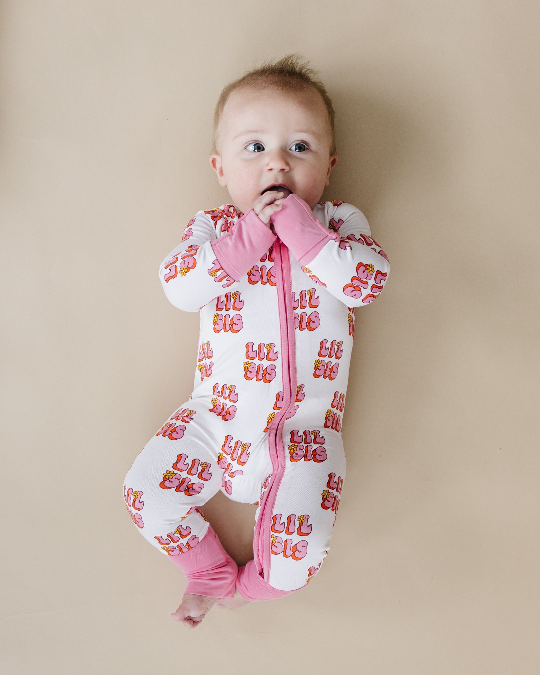 Baby wearing a white onesie with red text and pink accents on a beige background